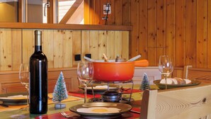 Een houten interieur met een eettafel gedekt voor twee personen, inclusief een fles wijn, een rode pan en borden met eten.