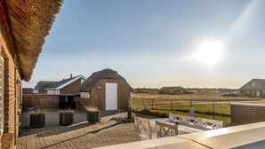 Un patio con muro de ladrillo, estructura de techo de paja y vistas al campo.