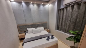A modern hotel room with a large bed, a bedside table, a nightstand, a potted plant, and a window with curtains. - Cairo Plaza Manchester Hotel (Cairo)