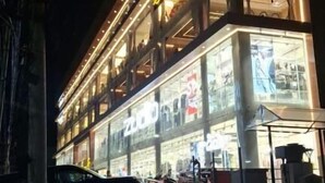 A multi-story building with illuminated signage, large windows, and parked cars in front. - Ricch Hotels (Hyderabad)