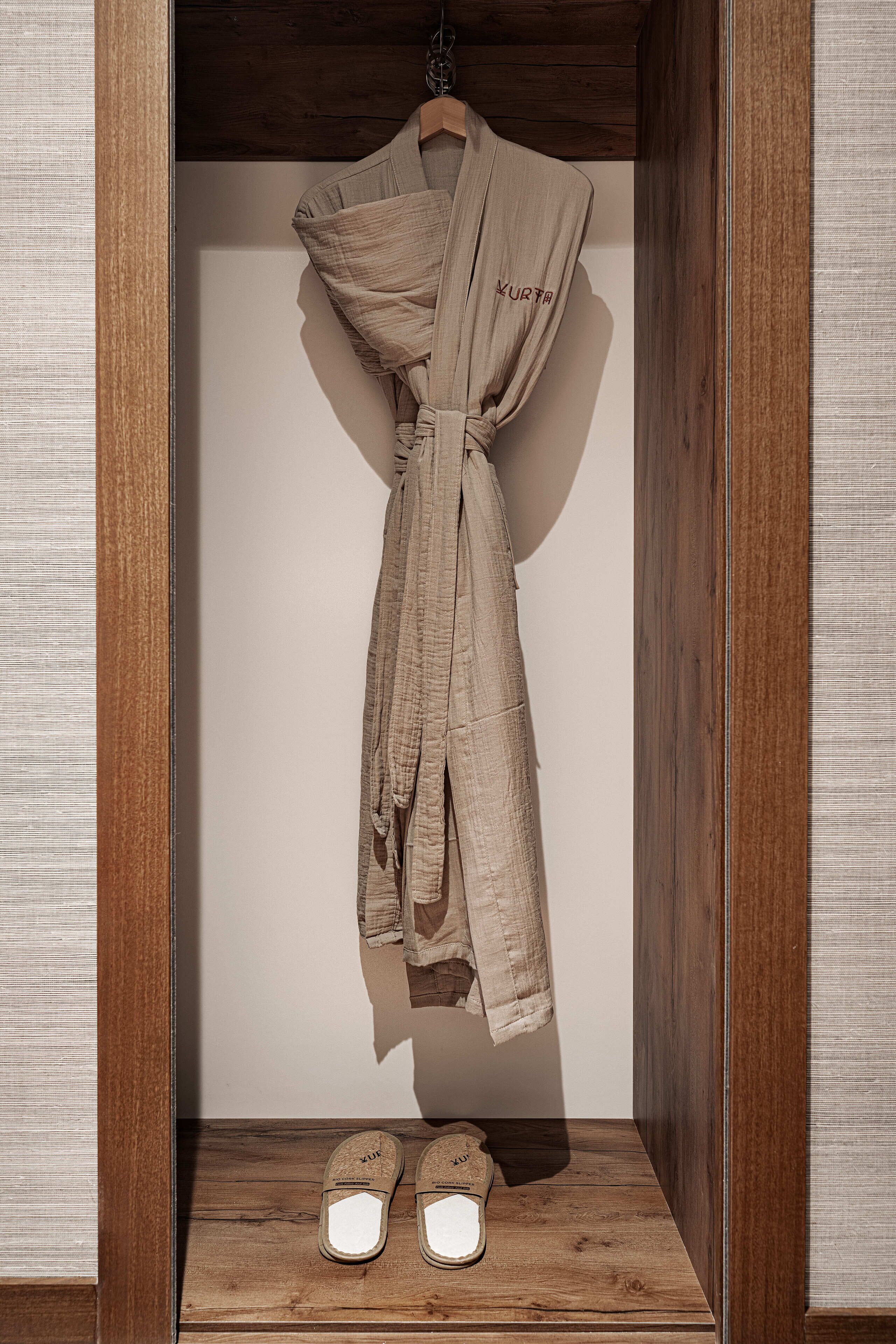 A wooden cabinet with a robe and slippers inside.