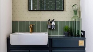 A bathroom with a white sink, dark cabinetry, a green hexagonal tile backsplash, and a mirror above the sink. - The Piggery - Pig 4 - Double Room (Reynoldston)