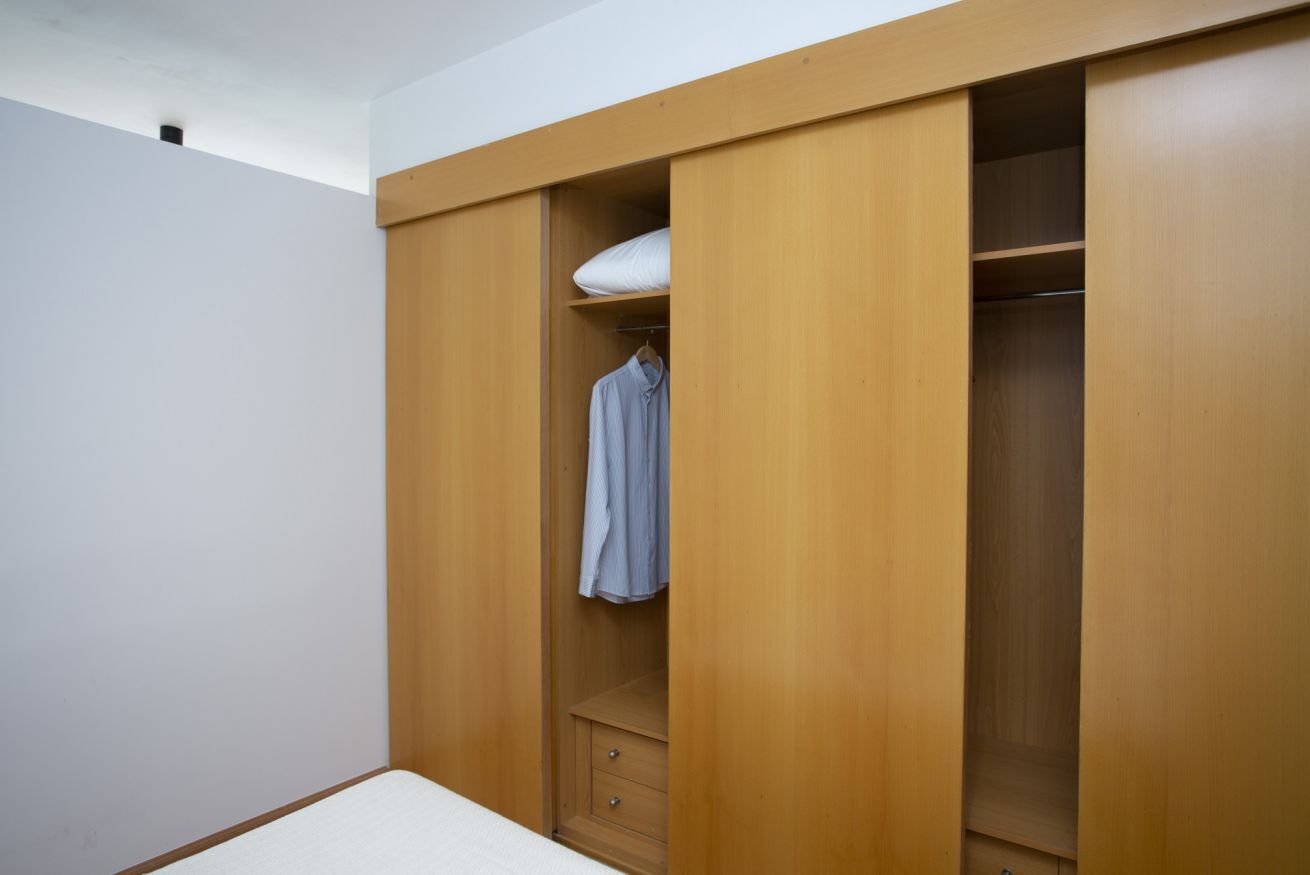 Une chambre à coucher avec une armoire en bois, une étagère suspendue et un lit.