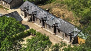 A long, narrow building with a sloped roof, likely a hotel or guesthouse, surrounded by trees and a paved area.