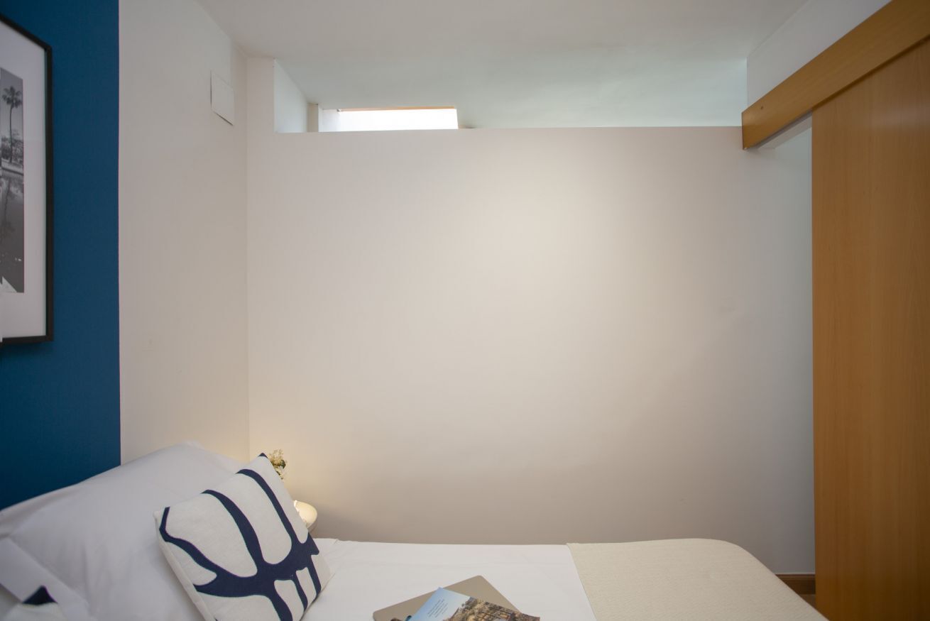 Ein Schlafzimmer mit einem Bett, einem Kissen, einem Nachttisch, einem gerahmten Bild an der Wand und einem Fenster.