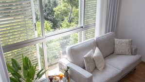 A living room with a sofa, a small table with a tray of food, a potted plant, and a view through large windows.