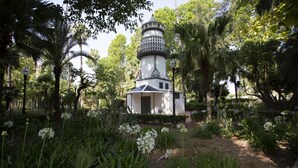 A white lighthouse with a black top, surrounded by lush greenery and flowering plants.