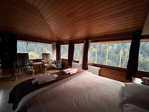 A wooden-paneled room with a bed, a desk, a chair, and a view of the forest through large windows. - Ayder Hotel (Çamlıhemşin)