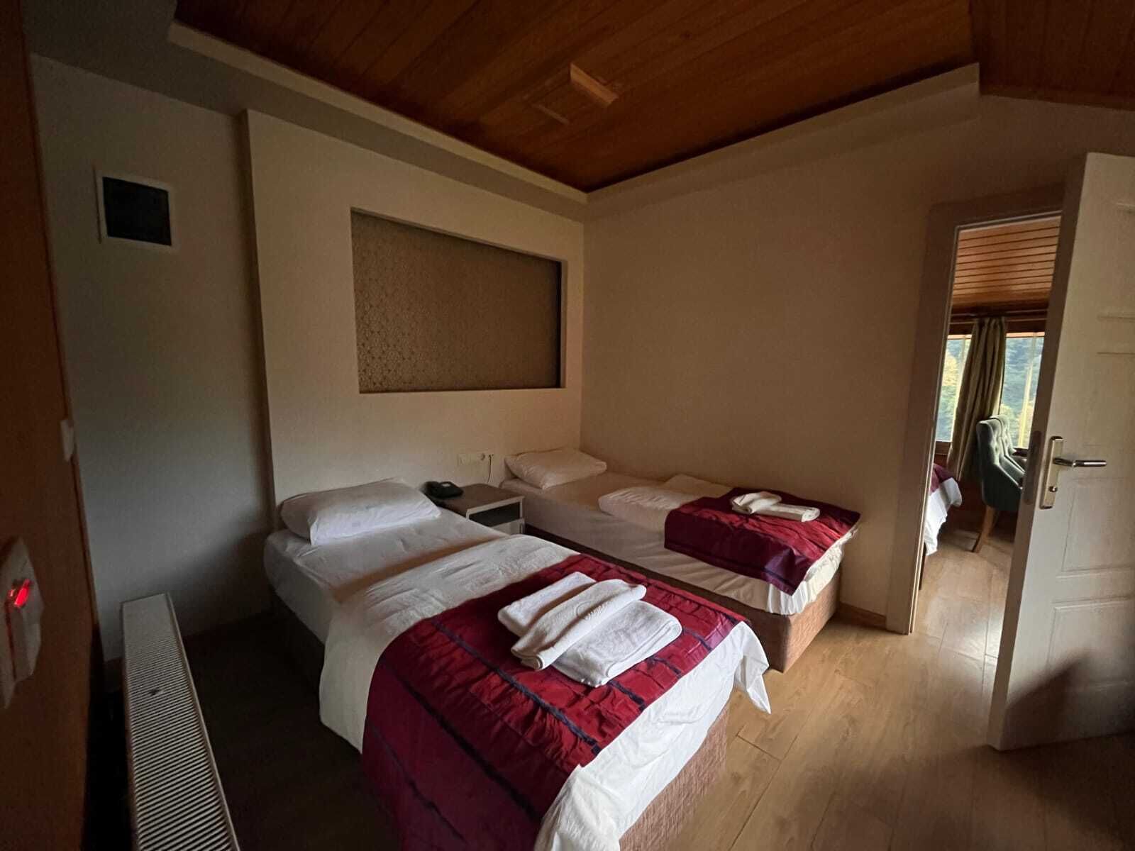 Een hotelkamer met twee bedden, een houten plafond en een raam met zonwering.
