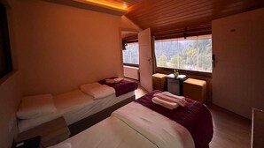 A room with two beds, a small table with bottles, and a window with a view of trees. - Ayder Hotel  (Çamlıhemşin)