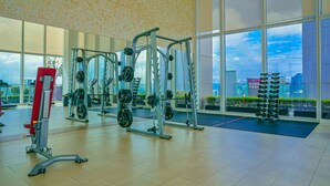 A gym with various exercise equipment, large windows, and a view of a cityscape. - The Platinum KLCC By Aura Suites (Kuala Lumpur)