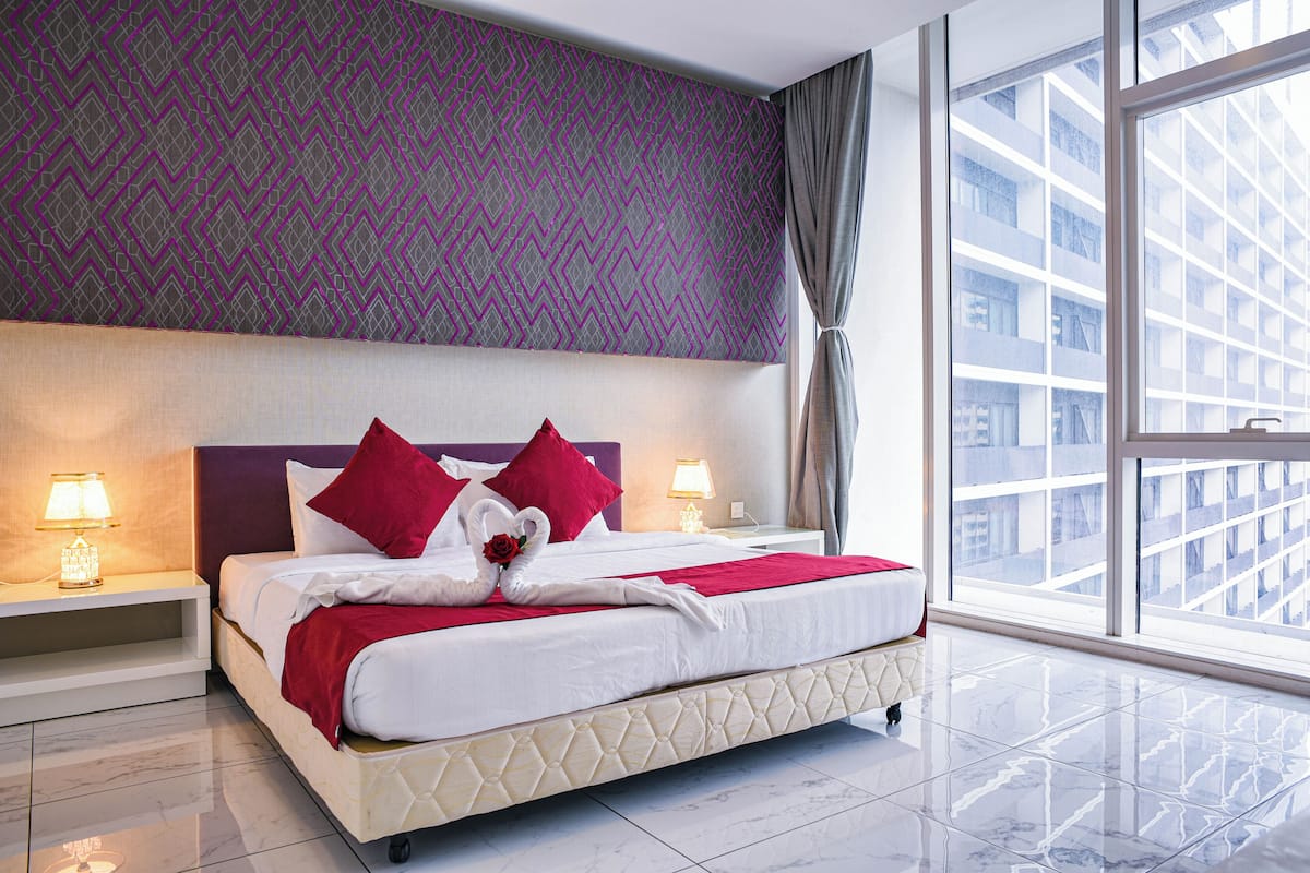 Ein modernes Hotelzimmer mit einem großen Bett, zwei Nachttischlampen, Blick auf die Stadt durch große Fenster und einer Wand mit Musterdesign.