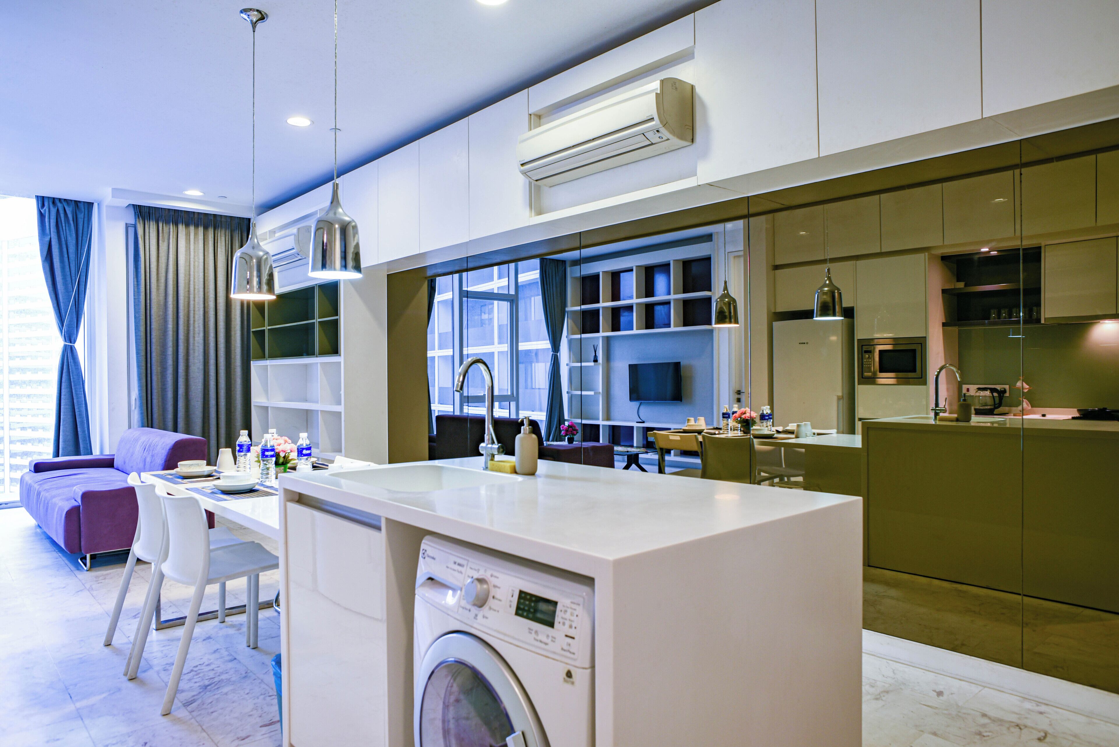 A modern kitchen with a built-in washing machine, a dining area with a table and chairs, and a living area with a sofa and a TV.