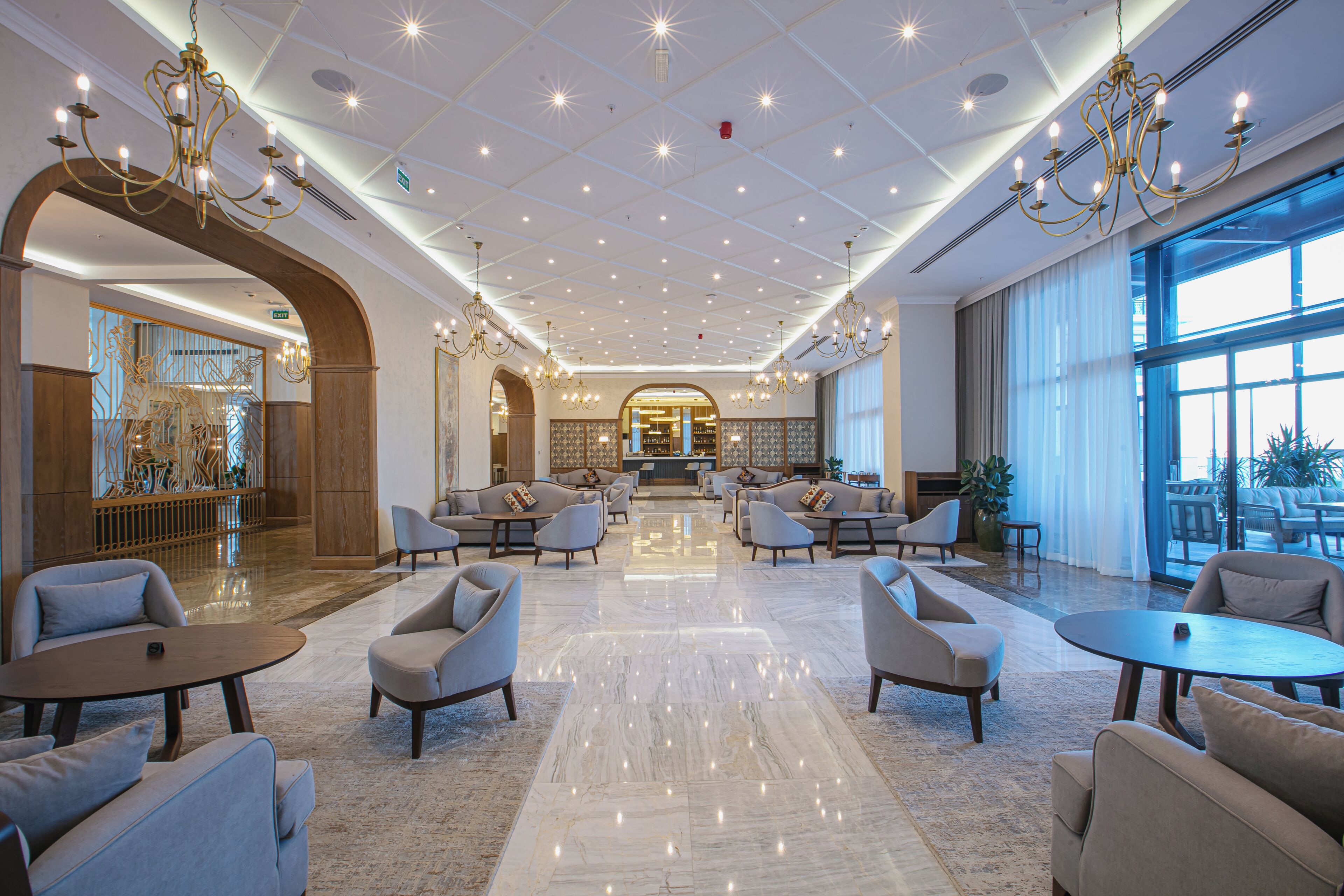 A spacious lobby with a high ceiling, chandeliers, and a central seating area with sofas and tables.