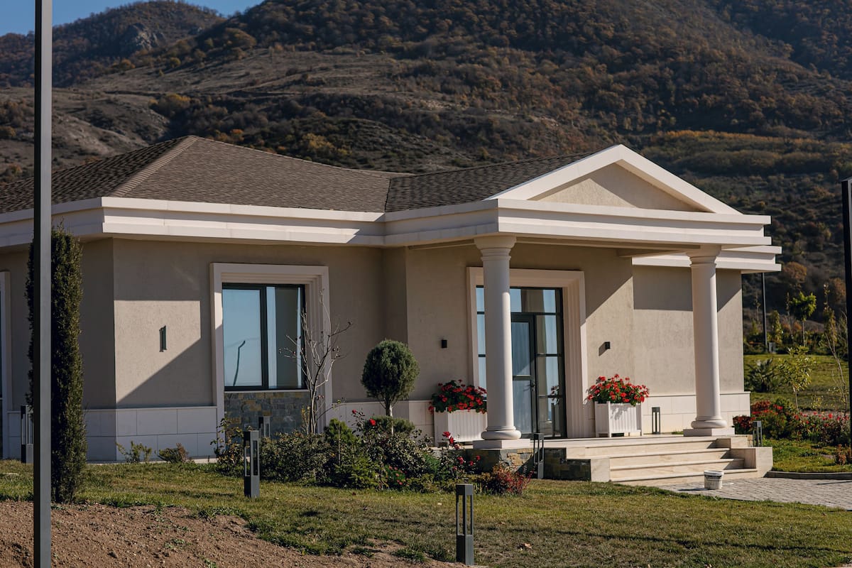 A two-story house with a front porch, columns, and a mountain backdrop.