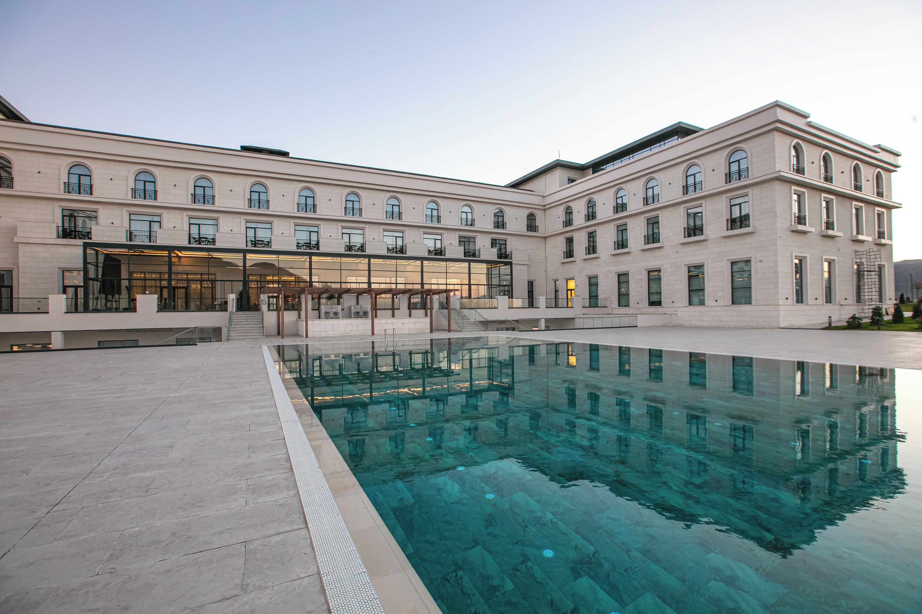 A building with a swimming pool, multiple windows, and a covered area with stairs leading to an entrance.