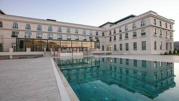 A building with a swimming pool, multiple windows, and a covered area with stairs leading to an entrance.