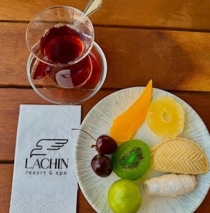 A plate with fruits and a glass of red beverage on a wooden table, next to a napkin with a logo. - Lachin Resort & SPA (Lachin)