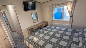 A bedroom with a bed, a TV mounted on the wall, a desk, and a window with curtains.