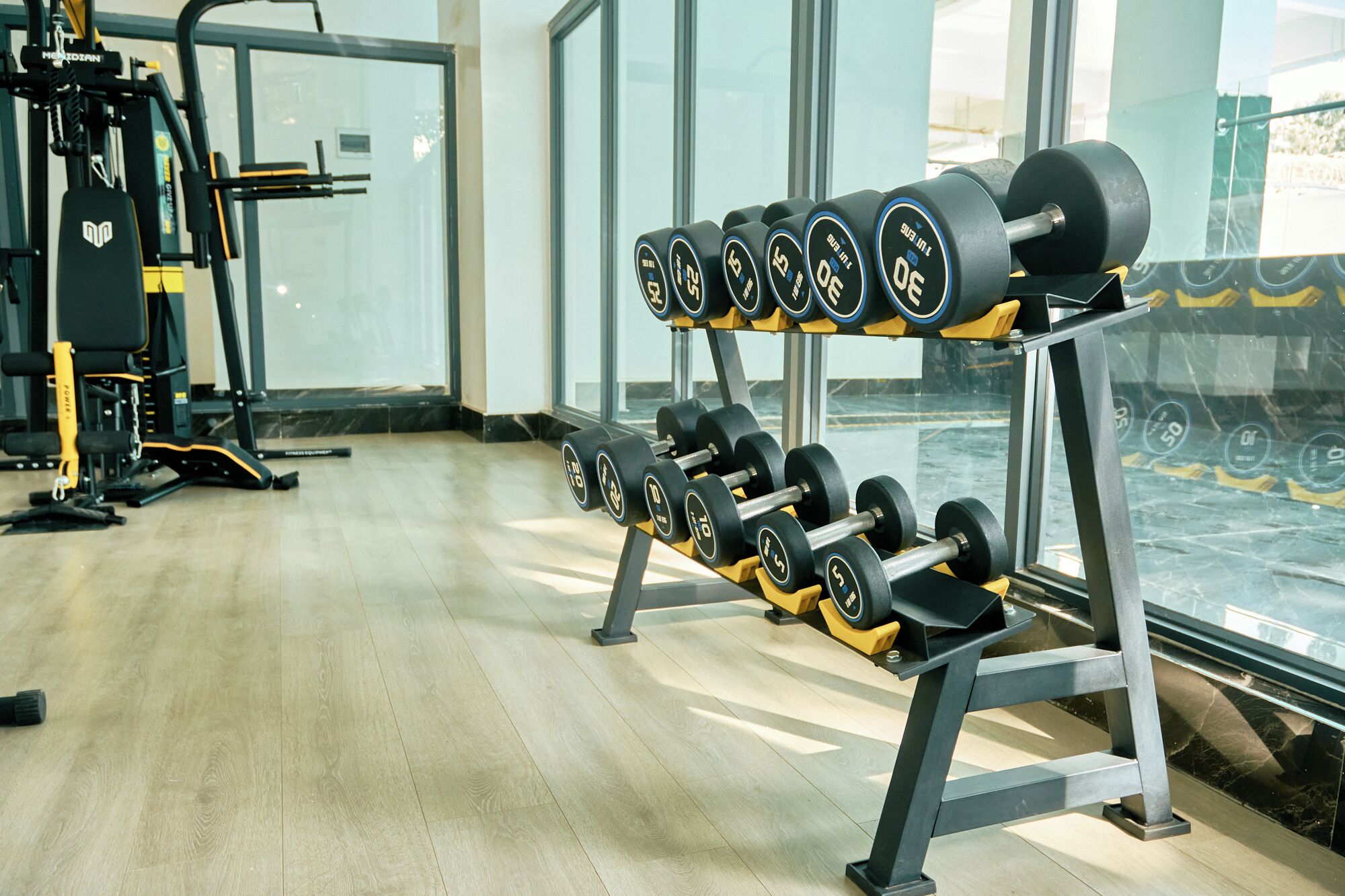 Een sportschool met gewichthefapparatuur, waaronder dumbbells en een bankdrukpers.