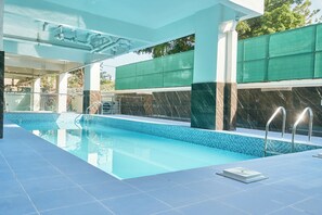 Ein beheiztes Hallenbad mit klarem, blauem Wasser, einer gefliesten Liegefläche und modernem Architekturstil.