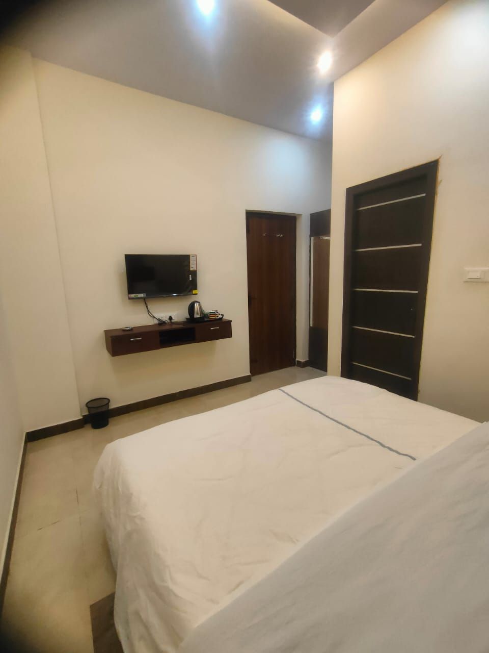 Un dormitorio con cama, televisión montada en la pared, puerta de madera y armario.