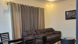 Ein modernes Wohnzimmer mit einem grauen Sofa, einem Esstisch mit Stühlen und einem Deckenventilator.
