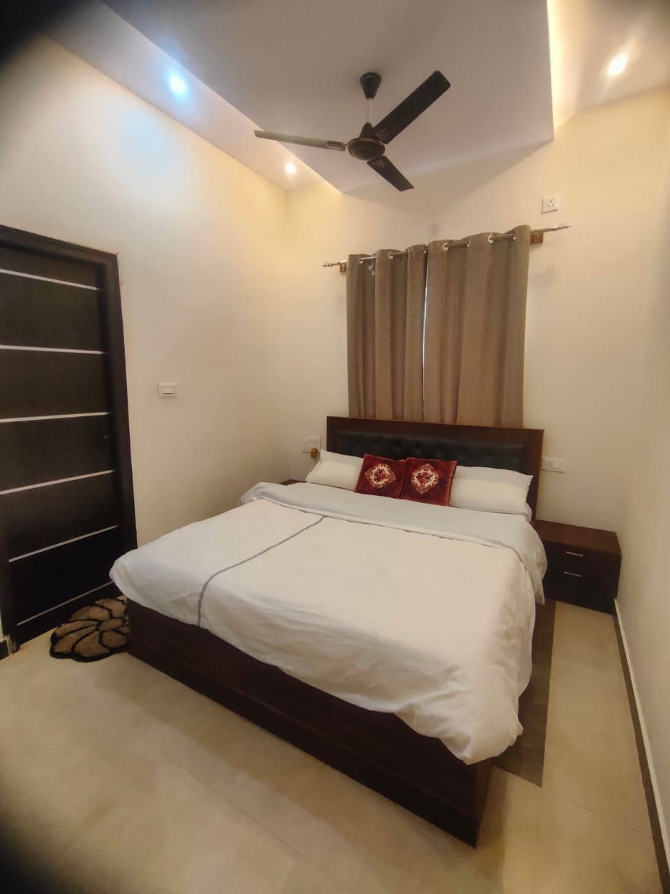 Un dormitorio con cama, ventilador de techo, ventana con cortinas y puerta.