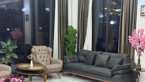 A modern living room with a grey sofa, a beige armchair, and a round coffee table. There are potted plants and a vase with flowers on the table. - BRB Hotel (Tbilisi)