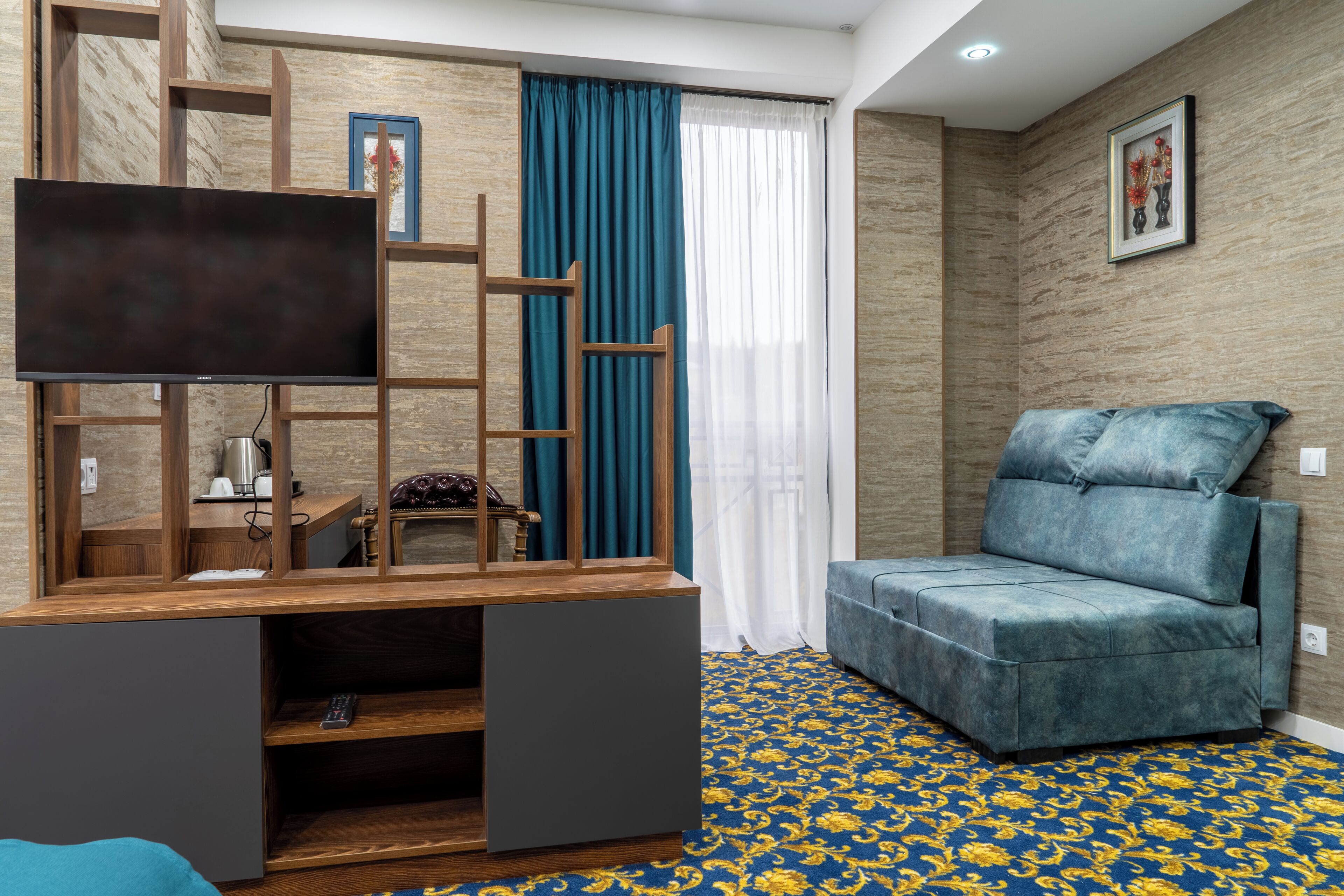 A modern living room with a TV on a wooden stand, a blue sofa, and a patterned carpet.