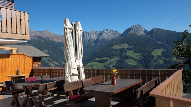Un espace extérieur aménagé avec des tables et des bancs en bois, une clôture en bois et une vue sur les montagnes en arrière-plan.