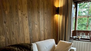 A cozy living room with a beige sofa, a fur throw, and a window with a view of greenery. - Alpine cocoon in Megève - charm, comfort & view (Megève)