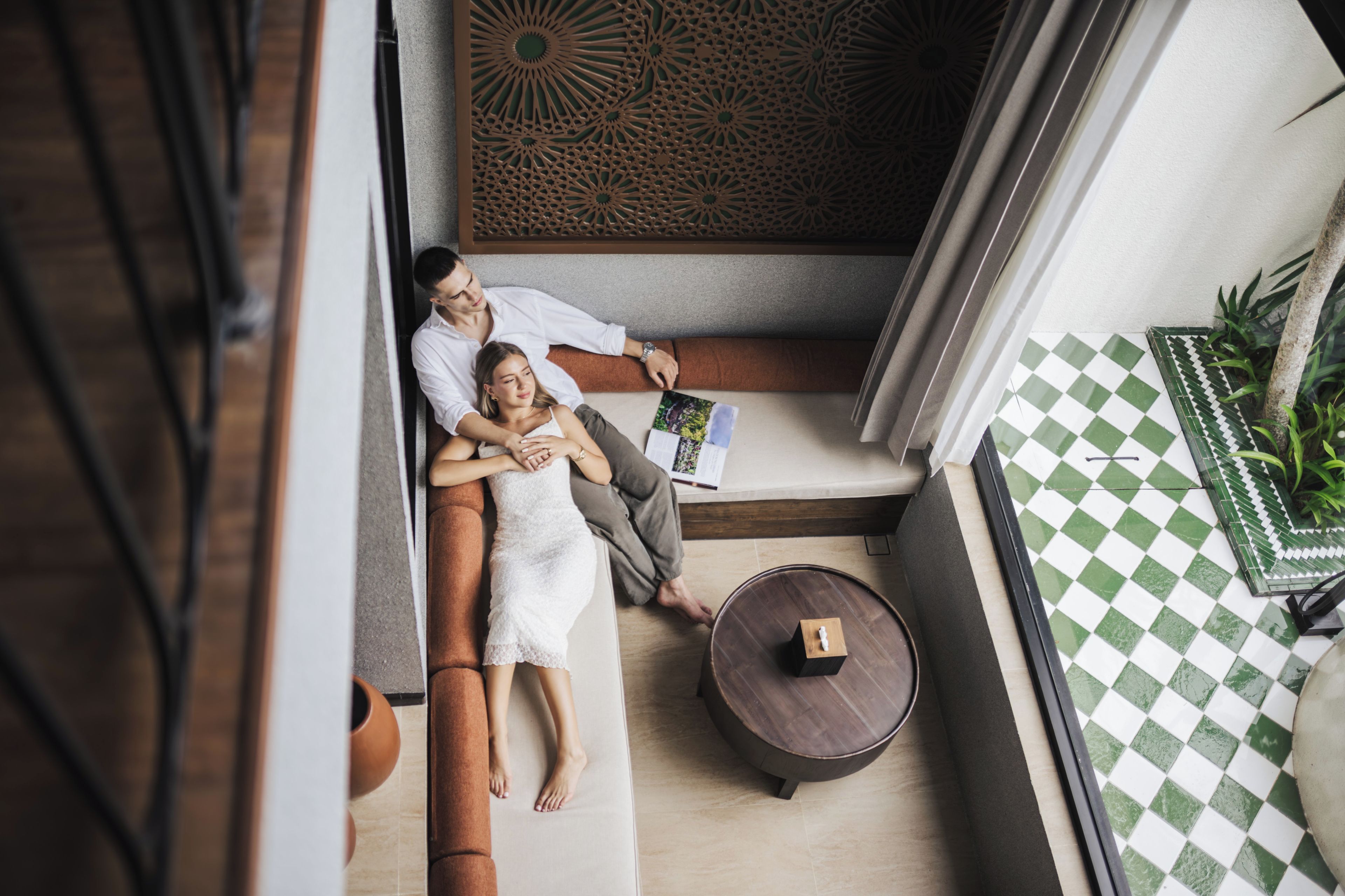 A couple relaxing on a sofa in a modern interior with a patterned wall and a checkered floor.
