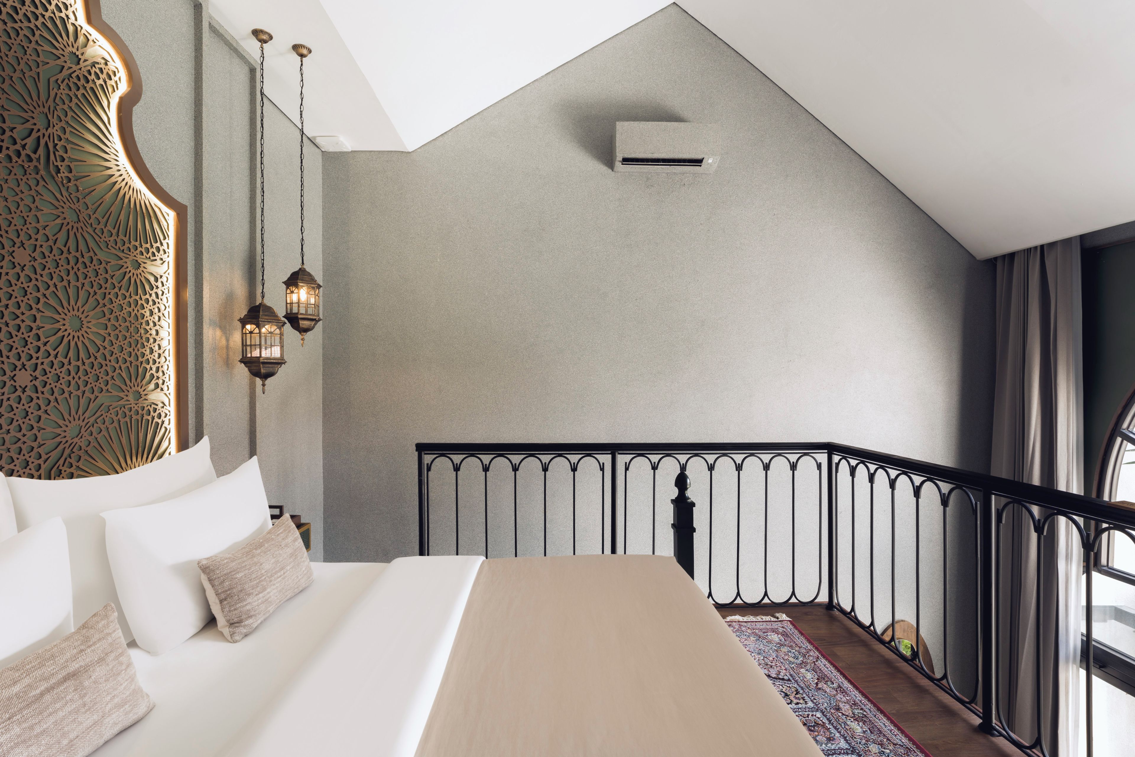 Un dormitorio con cama, un panel decorativo en la pared, faroles colgantes, una ventana y barandilla de balcón.