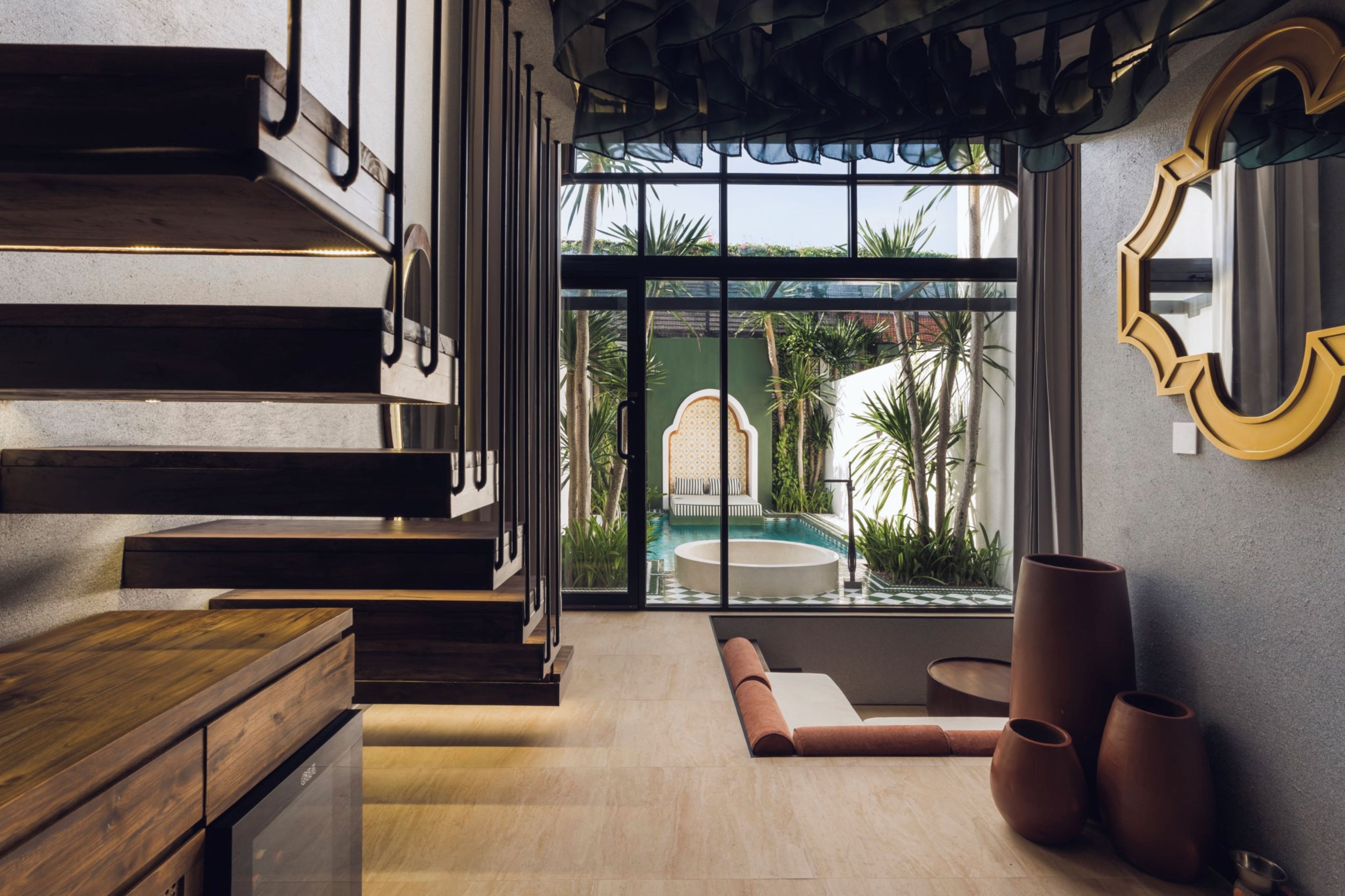 A modern interior with a wooden staircase, a pool visible through large windows, and a round seating area.