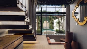A modern interior with a wooden staircase, a pool visible through large windows, and a round seating area.