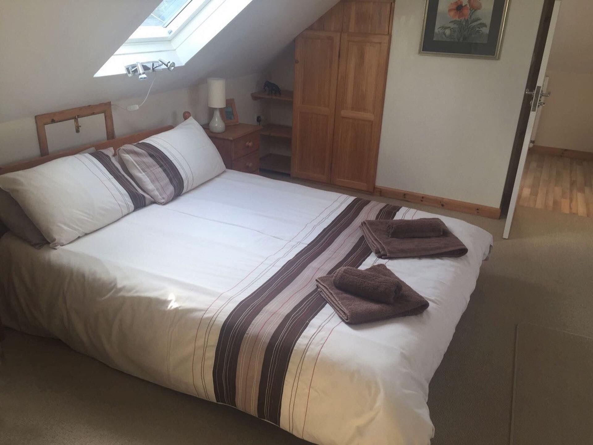 Une chambre à coucher avec un lit, une lucarne, une armoire en bois et un tableau encadré au mur.