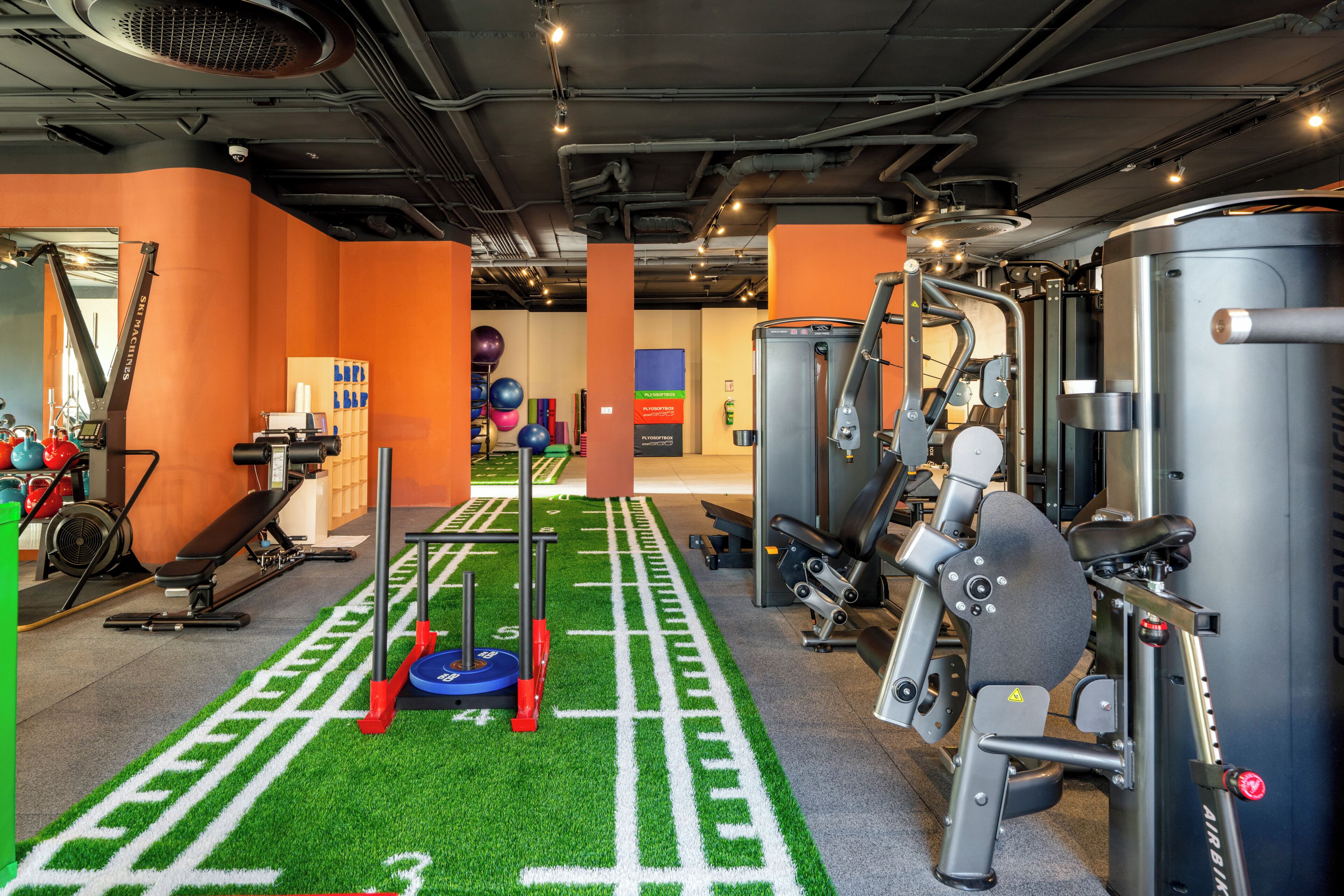A gym with exercise equipment, a green artificial turf area, and orange walls.