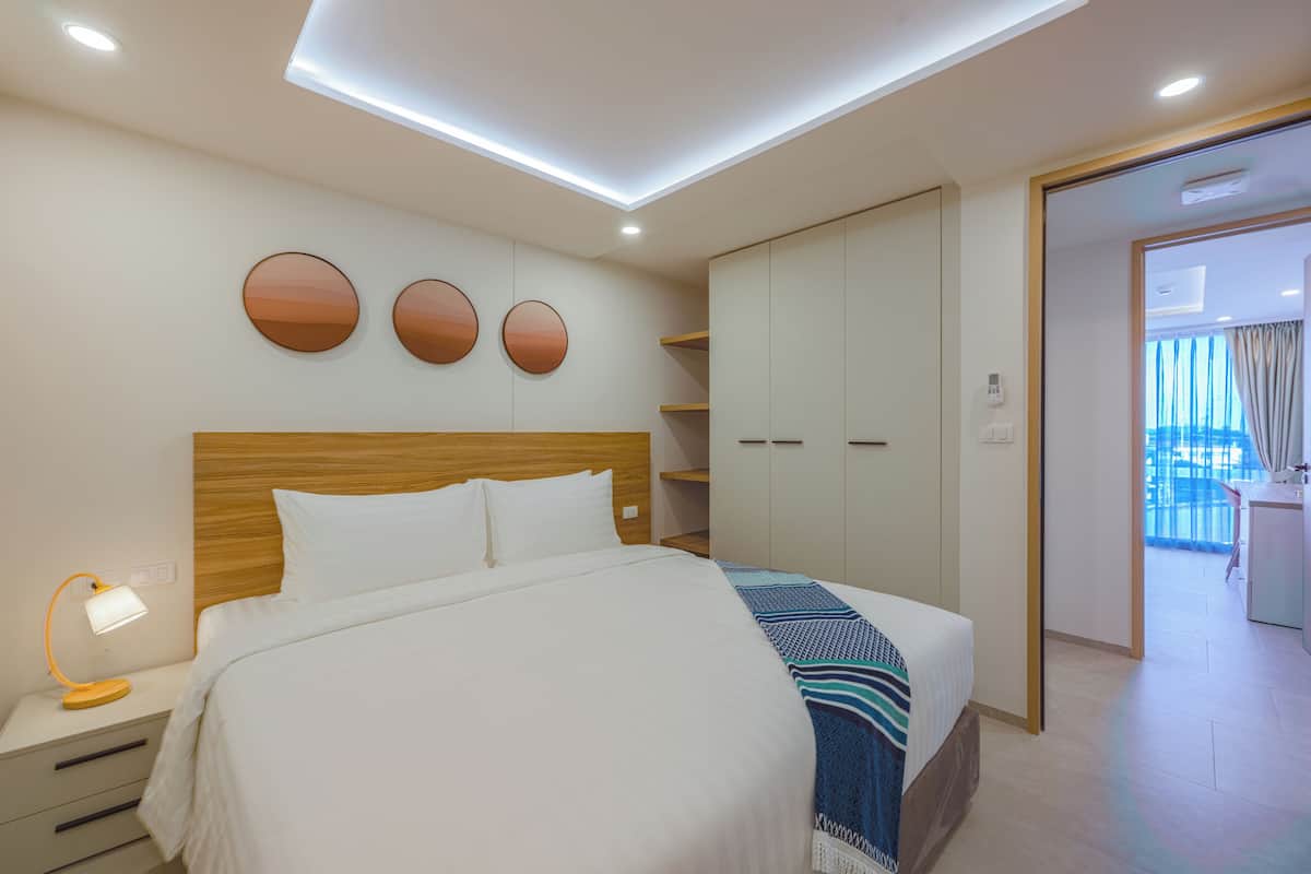 Una habitación de hotel moderna con una cama grande, mesitas de noche, un armario y vistas al balcón.