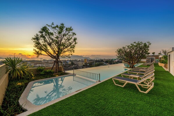 A rooftop pool with artificial grass, lounge chairs, and a view of the city skyline at sunset. - HOMA Chalong Bay (Chalong)