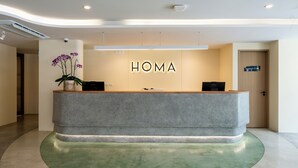 A reception desk with 'HOMA' signage, a potted orchid, and a green carpet. - HOMA Chalong Bay (Chalong)