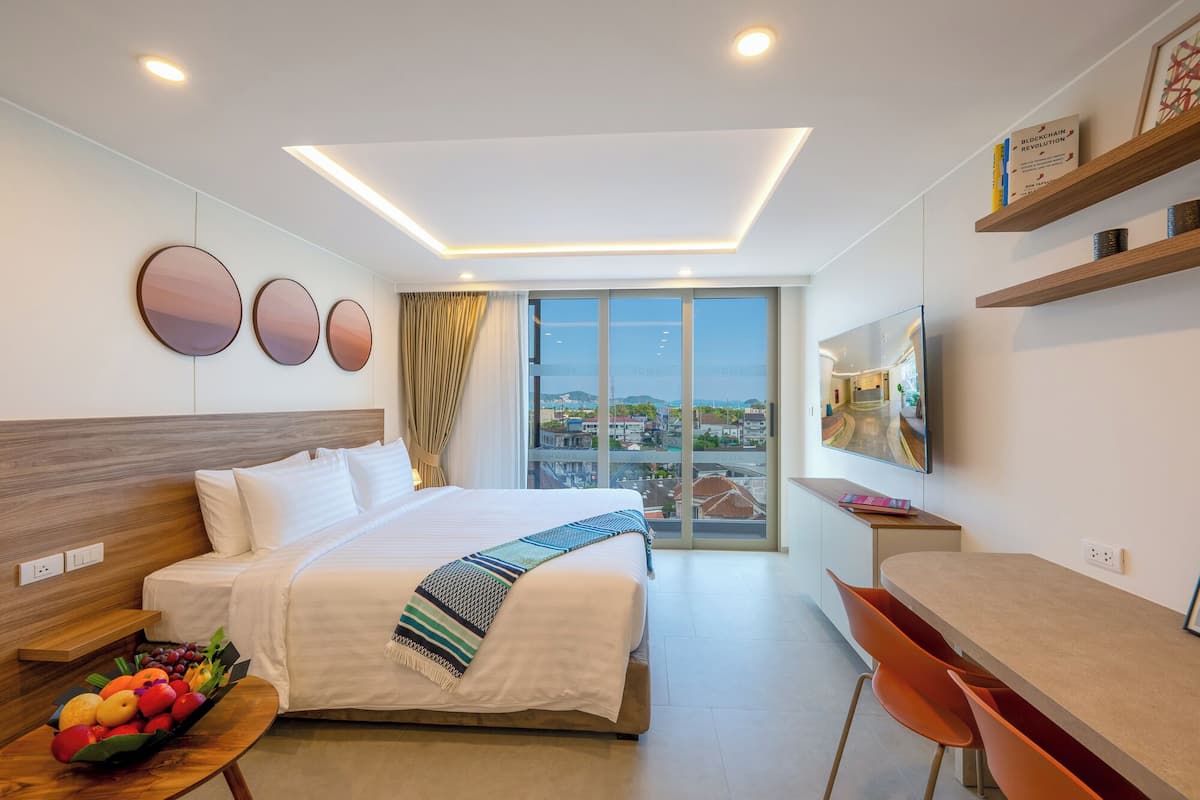 Una habitación de hotel moderna con una cama grande, un escritorio, una silla, un televisor y vistas a la ciudad.