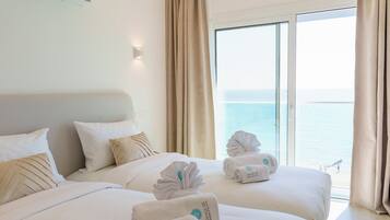 A hotel room with a bed, pillows, a wall-mounted air conditioner, and a view of the sea through a large window.