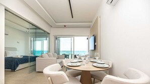 A modern hotel room with a balcony, a dining area, and a bed with a view of the sea. - Dinglis Beach Hotel Apartments (Larnaca)