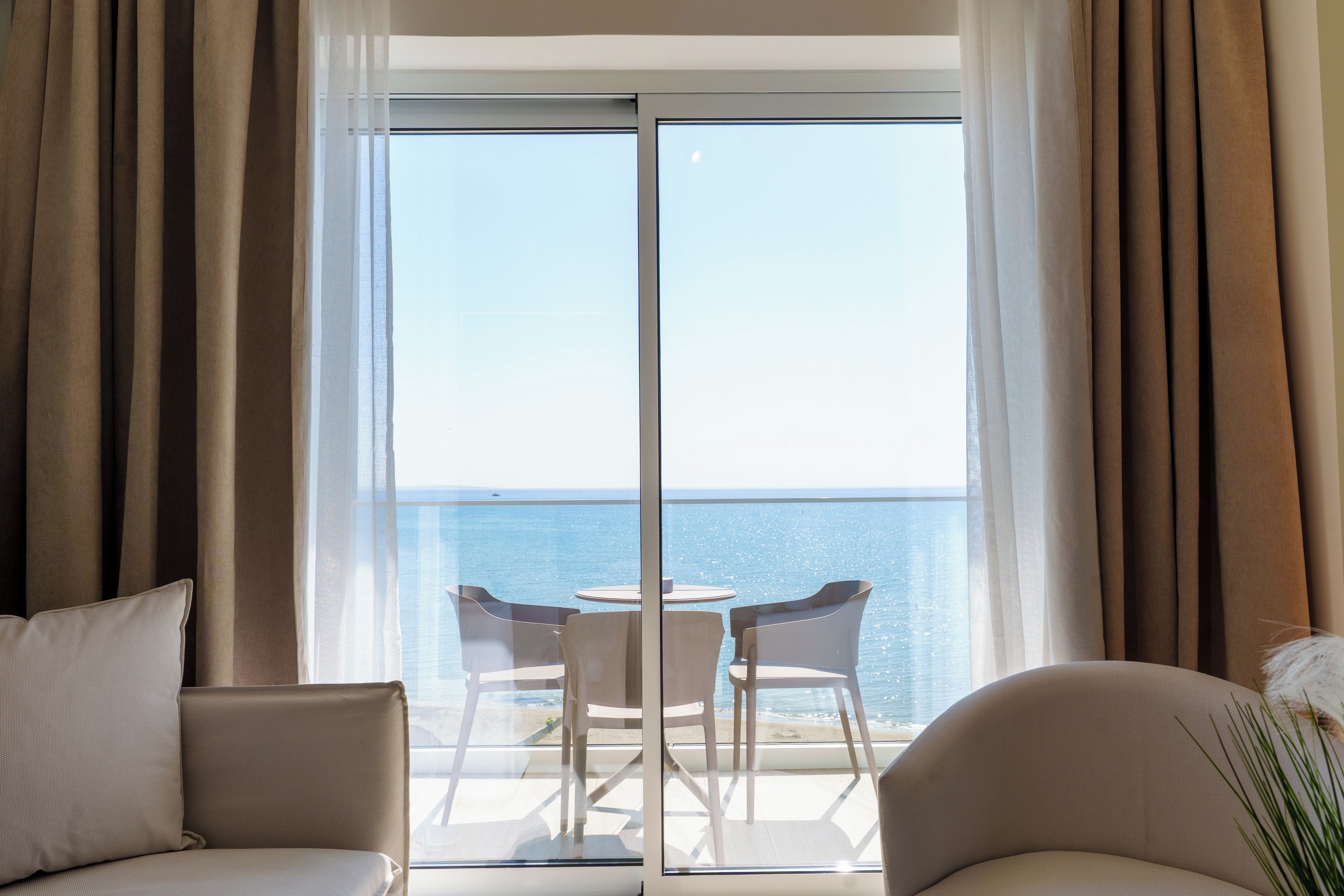 A room with a view of the sea through a large glass door, furnished with two chairs and a small table.