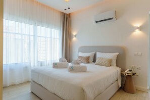 A hotel room with a large bed, a bedside table with a phone, and an air conditioning unit on the wall. - Dinglis Beach Hotel Suites (Larnaca)