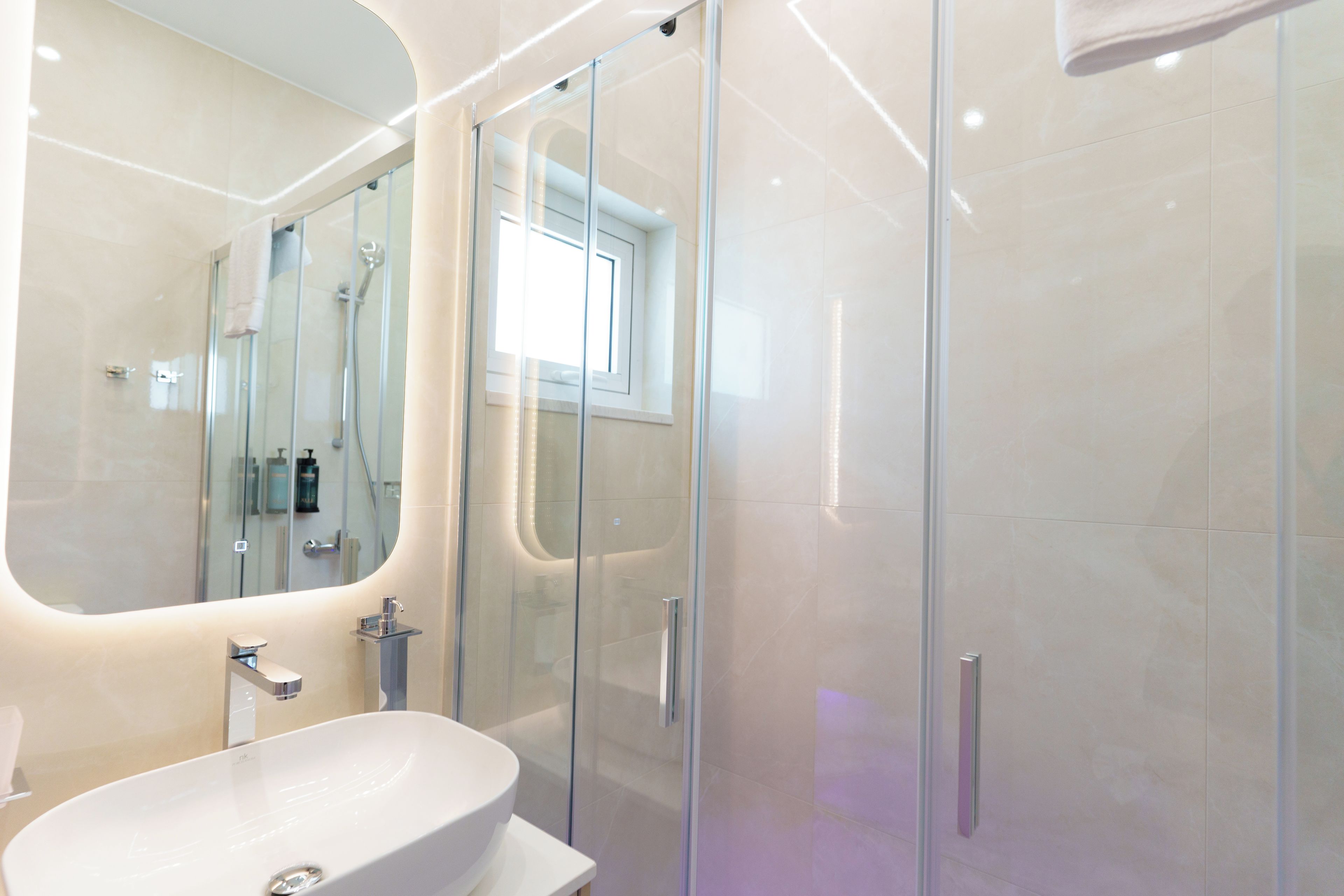 Un baño moderno con un espejo grande, ducha con cerramiento de vidrio y lavamanos blanco.