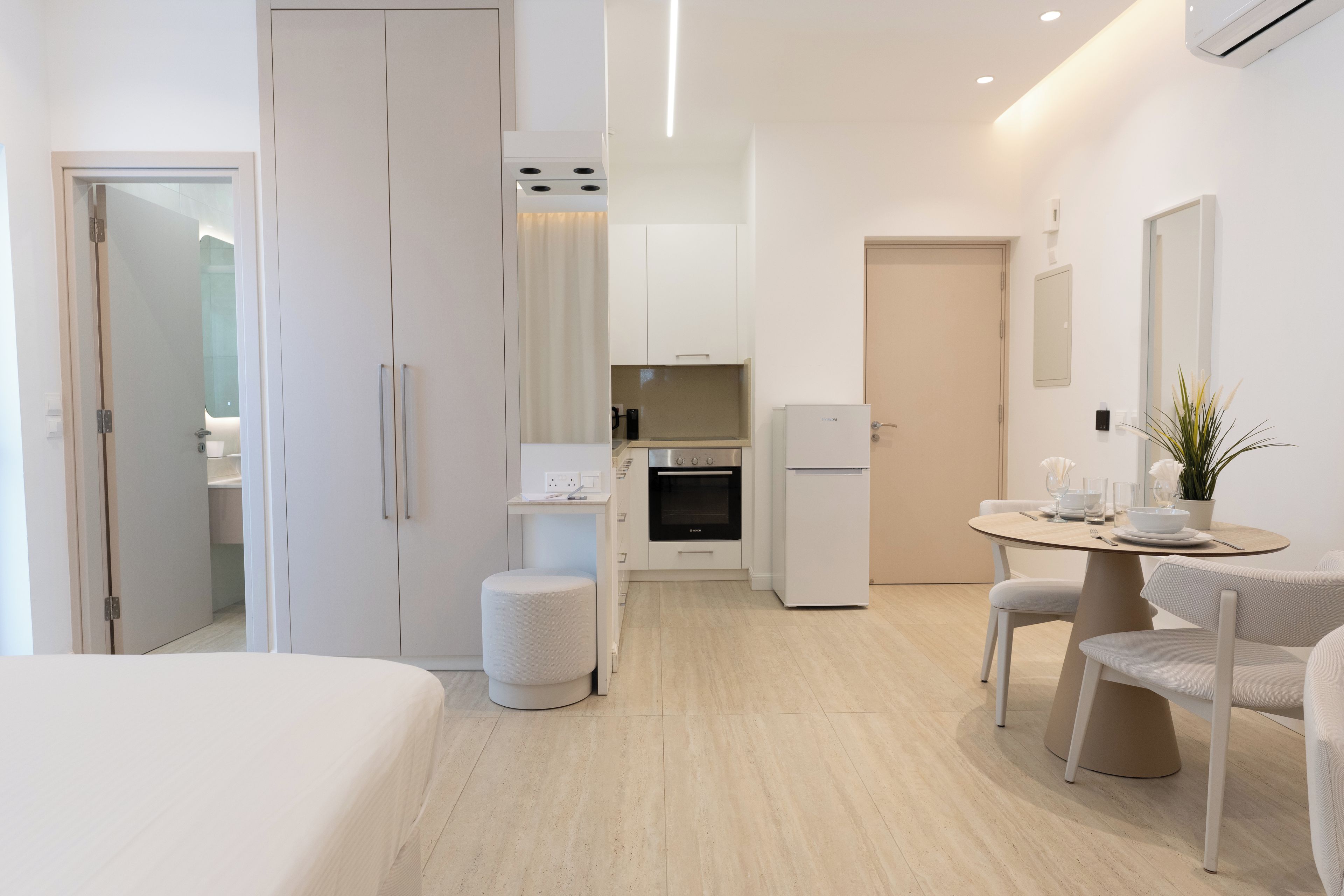 Una habitación de hotel moderna con cama, una kitchenette pequeña, un área de comedor con mesa y sillas, y un baño separado.