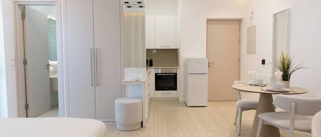 Una habitación de hotel moderna con cama, una kitchenette pequeña, un área de comedor con mesa y sillas, y un baño separado.