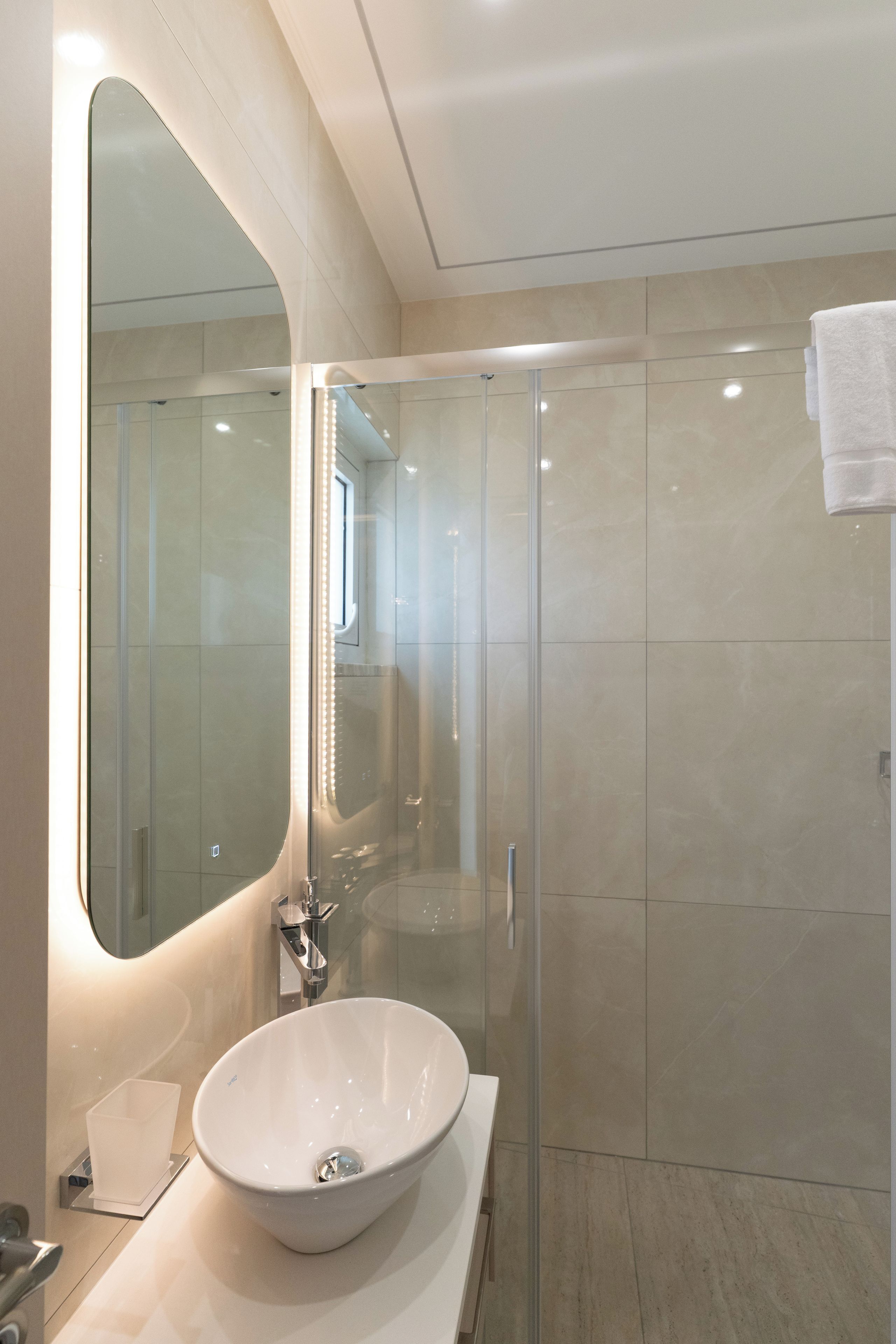 A modern bathroom with a large mirror, a glass-enclosed shower, and a white sink.